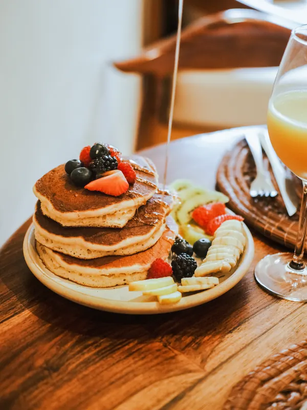 Une pile de pancakes aux fruits rouges, nappée de sirop, à côté d’un verre de jus.